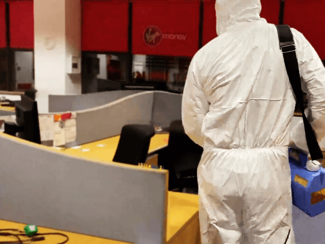 A employee wearing protective gear disinfecting an office area